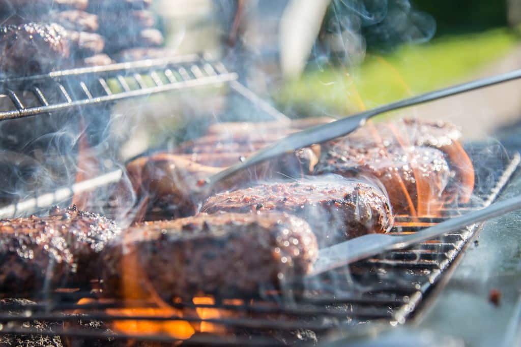 Turning a burger cooking on a grill with a kitchen tong