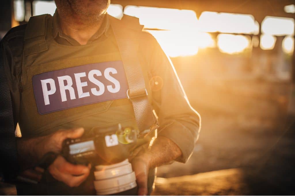 climate reporters; Journalist holding a camera and wearing a press vest